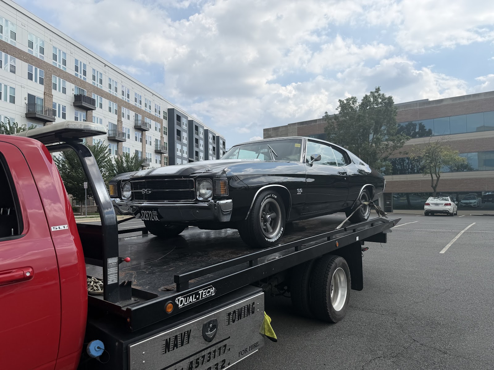 A black classic car on the bed of a Navy Towing truck